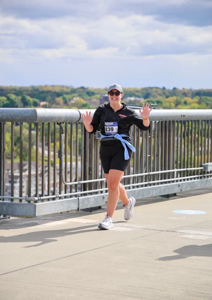 Lauren Sandford smiling and waving while running across a bridge during the Lehigh Valley Marathon